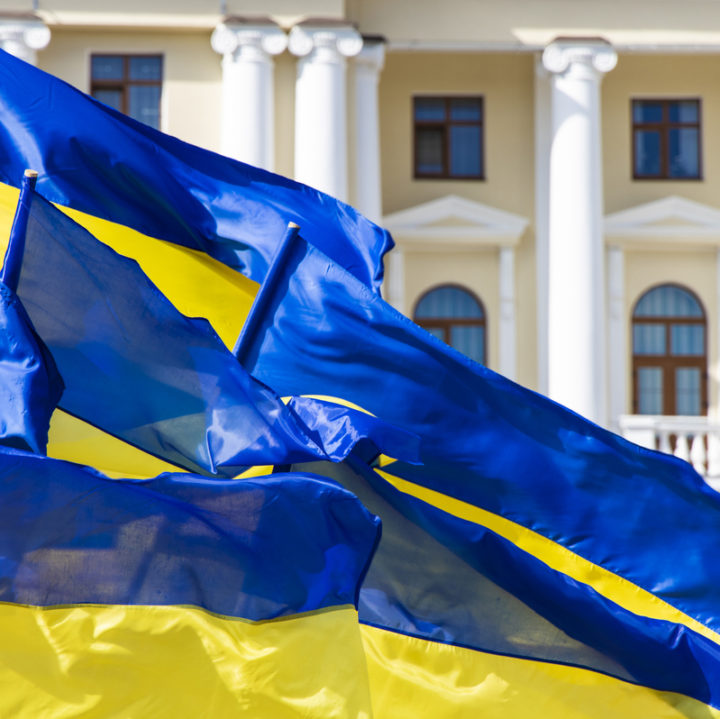 Ukraine blue yellow flags evolving on a wind near town hall classic architecture building with columns arch windows and soft pink and white walls, independence and revolution of dignity concept