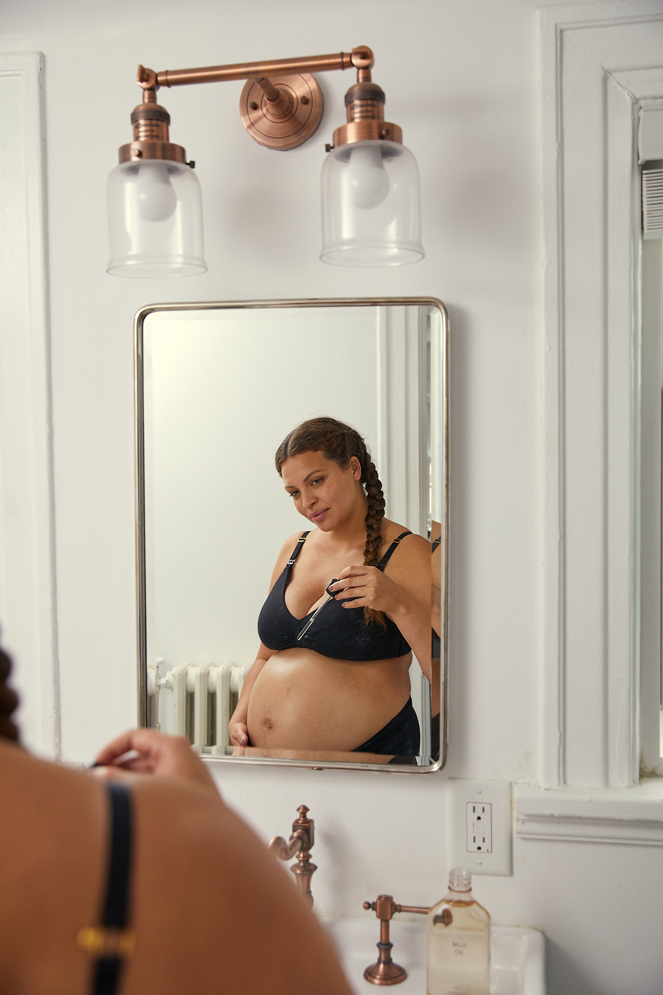 pregnant woman applying oil to her stomach in a mirror