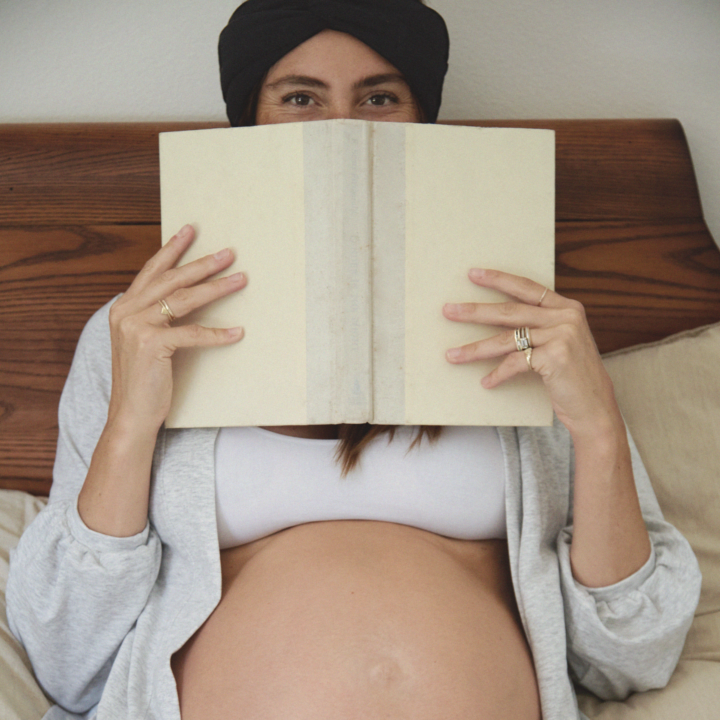 Pregnant woman holding a journal in front of her face.
